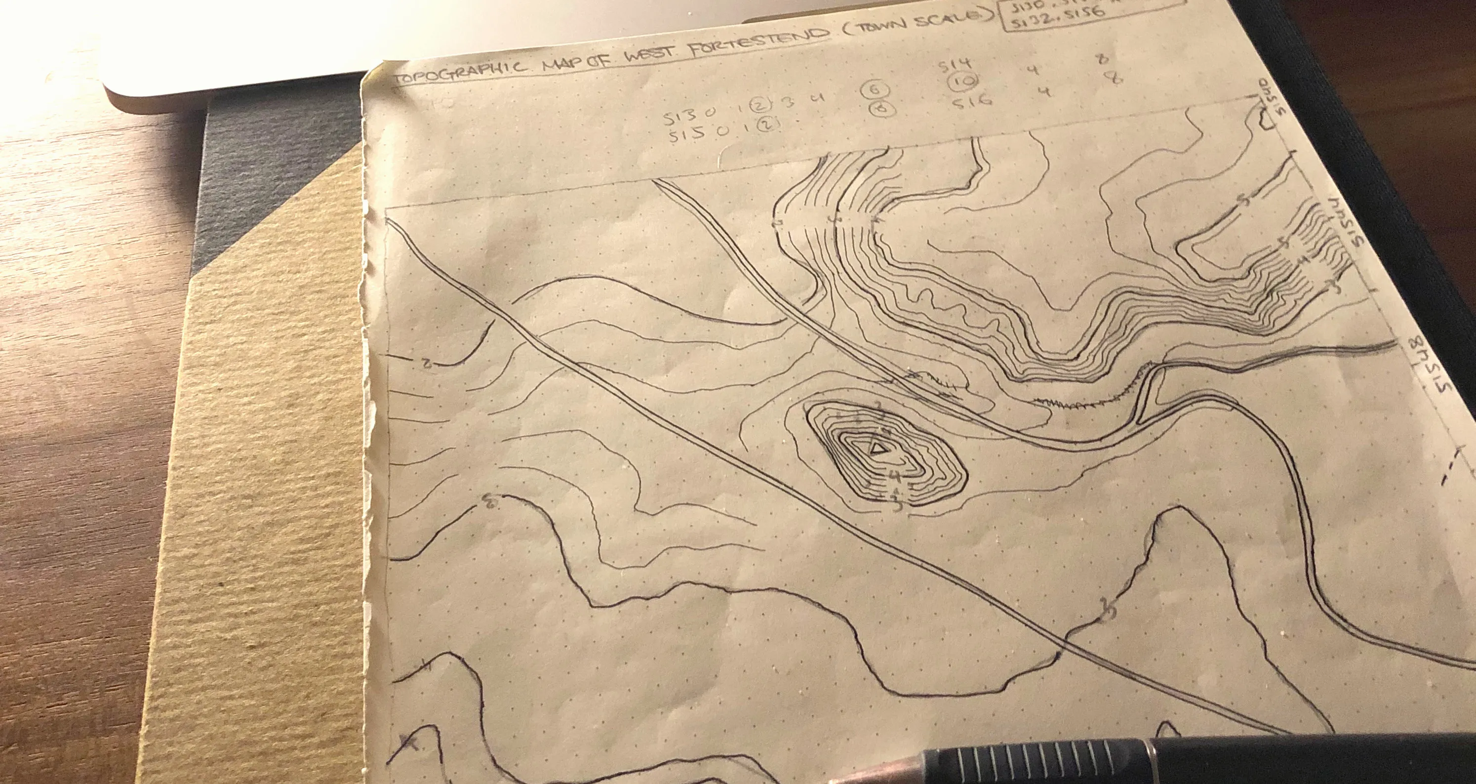 Photo of wooden desktop with hand-drawn, paper map and edge of laptop