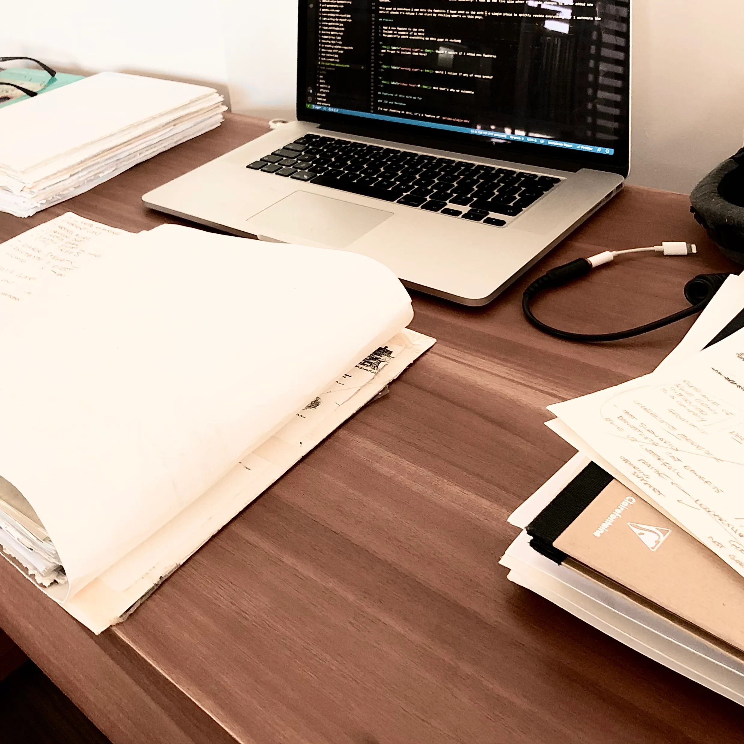 Stylised photograph, with slightly skewed angles, high contrast with muted colours. A desk with a laptop and stacks of paper